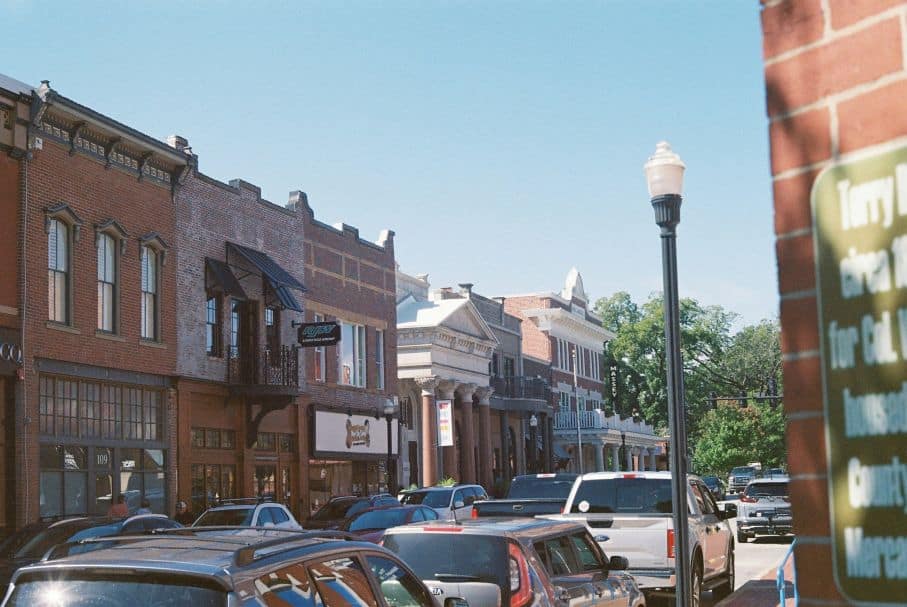A picturesque street view of a small town reveals historic brick buildings, parked cars, and a row of charming shops under the bright blue sky, presenting a perfect post template for capturing timeless community vibes.